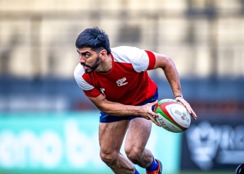 Intense rugby match with player running for a pass on the field.